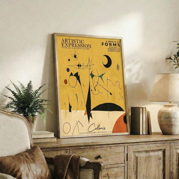 May include: Abstract art poster with yellow and cream background featuring black geometric shapes, orange accents, and flowing lines in mid-century modern style. Framed print displayed on rustic wooden sideboard alongside fern plant, ceramic vases, and books in neutral-toned living room setting.