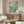 May include: Vintage-style poster with turquoise water showing three swimmers diving and floating, red "DEEP DIVE" text at bottom, displayed above walnut wood credenza in modern living room with white curved chair, glass coffee table, and minimalist white table lamp