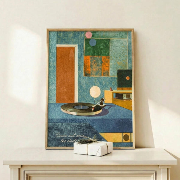 May include: Framed mid-century modern style poster with geometric shapes in blue, orange, and green tones featuring a vinyl record turntable scene. French text reads "Douce nuit sous les étoiles" at bottom. Artwork displayed on light wood shelf next to small wrapped white gift box with natural twine and dried sprig against cream wall.