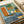 Abstract modernist artwork featuring geometric shapes in blue, green, orange and yellow tones. A silhouetted figure paddles a canoe across layered rectangular forms suggesting a dreamlike landscape. French text "Douce nuit sous les etoiles" appears at bottom. The print has a vintage textured appearance and is shown lying flat on white paper with rolled paper visible in background.