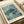 May include: Vintage-style art print featuring a detailed sea turtle swimming among coral and marine plants in muted green and teal tones. The poster displays "YAYOI KUSAMA" at the top, "1966" and "Modern Art" at the bottom, with cream borders. Print sits on white paper with neutral ribbon nearby on a light wooden surface.