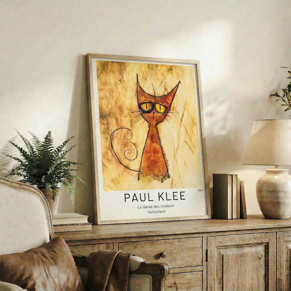 May include: Framed art print featuring a stylized orange cat with pointed ears, yellow eyes, and curved tail on weathered golden background, displayed on rustic wooden sideboard alongside fern plant, ceramic vase, and stacked books in warm neutral living room setting.