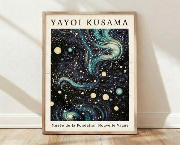 May include: A framed poster featuring a cosmic abstract artwork with swirling turquoise and navy blue patterns resembling galaxies, scattered with cream and teal circular dots like stars and planets against a dark starry background. The print has "YAYOI KUSAMA" at the top and "Musée de la Fondation Nouvelle Vague" at the bottom in black text on white borders. Displayed in a light wood frame leaning against a white wall on wooden flooring with soft natural lighting.