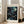 May include: Framed art print with cosmic swirling patterns in deep blues and teals against black starry background, featuring floating circles in cream and turquoise. Light wood frame leaning against white wall next to beige upholstered chair in bright room with large windows and natural lighting.