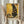 May include: Person holding framed art print in cream-colored wooden frame, featuring black cat in Gustav Klimt's golden decorative style with circular patterns and geometric designs. Print displays text "NINE LIVES OF LUXURY" and "NO PAWS IN MY PLANS, ONLY PURRFECTION" below artwork. Person wears beige ruffled sleeve top, holds dried pampas grass, standing against white curtained window background.