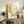 May include: Framed Picasso-style minimalist poster with yellow geometric shape, black lines, and red coffee cup on cream background, displayed on rustic wooden sideboard alongside fern plant, ceramic vases, and books in warm-toned living room setting