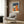 May include: Modern living room with beige armchair featuring geometric patterned pillow, brass floor lamp, and framed Bauhaus poster on wood-paneled wall. Poster displays abstract architectural forms in orange, blue, and cream colors with "BAUHAUS" and "ARCHITECTURE 1919" text on navy background in light wood frame.