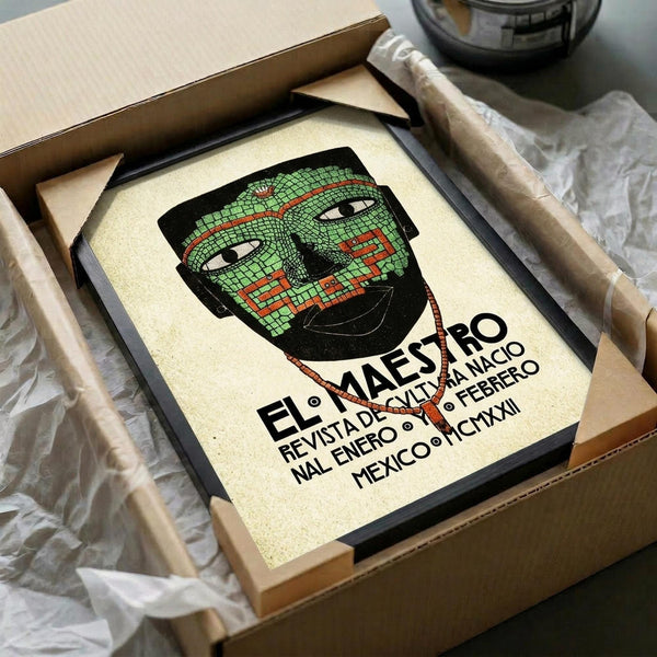 May include: Framed vintage-style poster featuring green mosaic-patterned mask design with red geometric details and Spanish text below. Print displayed in black frame inside opened cardboard shipping box with brown packing paper and protective wrapping materials visible around edges.