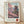 May include: Framed poster print leaning against white wall on light wood floor, showing Japanese pagoda temple with pink cherry blossom trees in traditional woodblock print style, featuring Japanese text on left side and "SAKURA" with red circular stamp at bottom, displayed in natural wood frame