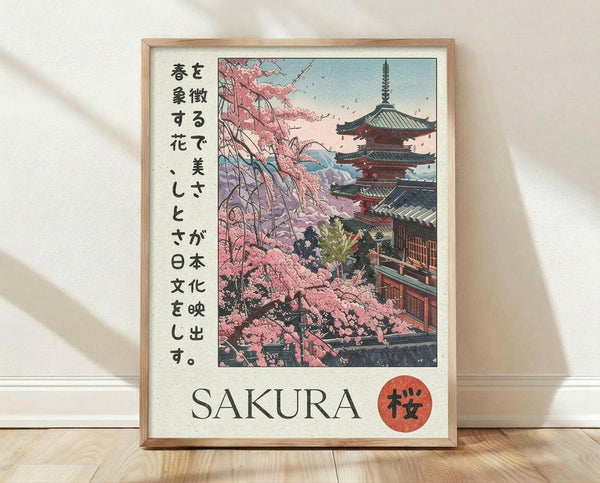 May include: Framed poster print leaning against white wall on light wood floor, showing Japanese pagoda temple with pink cherry blossom trees in traditional woodblock print style, featuring Japanese text on left side and "SAKURA" with red circular stamp at bottom, displayed in natural wood frame