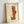 May include: A framed abstract art print leaning against a white wall on a white surface. The artwork features geometric shapes in warm orange and brown tones with a small blue accent, combined with delicate line drawings on an aged cream background. The piece is titled "PAUL KLEE" at the top with "Switzerland" and "1924" at the bottom. The print is displayed in a thin light wood frame.