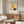May include: Framed vintage-style poster featuring woman in golden yellow cloche hat smelling deep red rose, displayed above walnut wood credenza in modern living room with cream upholstered chair, glass coffee table, and minimalist decor in neutral tones