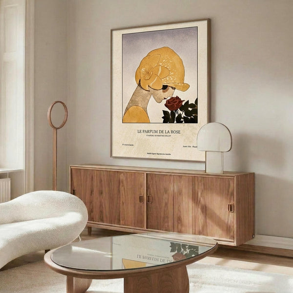 May include: Framed vintage-style poster featuring woman in golden yellow cloche hat smelling deep red rose, displayed above walnut wood credenza in modern living room with cream upholstered chair, glass coffee table, and minimalist decor in neutral tones