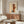 May include: Paul Klee abstract art poster in wooden frame hanging above mid-century walnut credenza in modern living room. Artwork features geometric shapes in warm orange, brown and blue tones with linear elements on cream background. Room styled with white curved chair, glass coffee table, and brass floor and table lamps creating soft lighting on neutral walls.