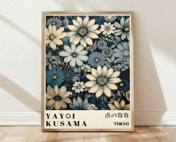 May include: Framed botanical art print featuring densely packed flowers in cream, white, and blue tones against a dark navy background. The artwork shows daisy-like blooms with detailed centers in a vintage illustrative style. Below the floral design is text reading "YAYOI KUSAMA" and Japanese characters, with "TOKYO" in the corner. The print sits in a light wood frame on wooden flooring against a white textured wall with soft natural lighting.