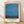 May include: Framed poster print featuring an abstract color field painting with horizontal bands of blue and teal tones, bordered by coral and red edges. The cream-colored poster displays "THE MODERNIST ARCHIVE" and "MARK ROTHKO" text below the artwork, along with "HISTORY OF PAINTING", "MODERN ART", "CHROMA STUDIES" and "1950s". Light wood frame rests against white textured wall on light wooden flooring with natural shadows.
