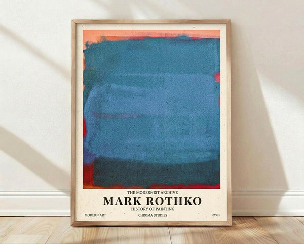 May include: Framed poster print featuring an abstract color field painting with horizontal bands of blue and teal tones, bordered by coral and red edges. The cream-colored poster displays "THE MODERNIST ARCHIVE" and "MARK ROTHKO" text below the artwork, along with "HISTORY OF PAINTING", "MODERN ART", "CHROMA STUDIES" and "1950s". Light wood frame rests against white textured wall on light wooden flooring with natural shadows.