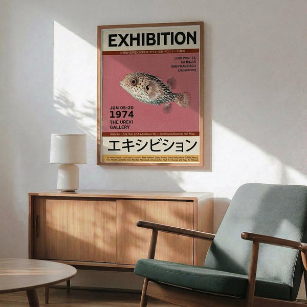 May include: Framed exhibition poster featuring a detailed pufferfish illustration on pink background with black text and Japanese characters, displayed above mid-century modern wooden credenza with white ceramic lamp, alongside sage green upholstered armchair with wooden frame in sunlit room with white walls.