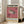 May include: Framed vintage-style exhibition poster leaning against beige couch in bright living room. Pink and cream poster features detailed pufferfish illustration with black text in English and Japanese characters. Natural wood frame, hardwood floors, large windows with sunlight streaming in.