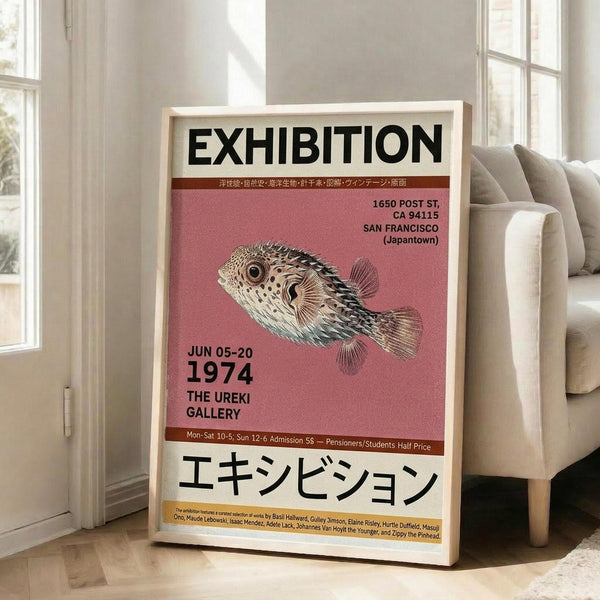 May include: Framed vintage-style exhibition poster leaning against beige couch in bright living room. Pink and cream poster features detailed pufferfish illustration with black text in English and Japanese characters. Natural wood frame, hardwood floors, large windows with sunlight streaming in.