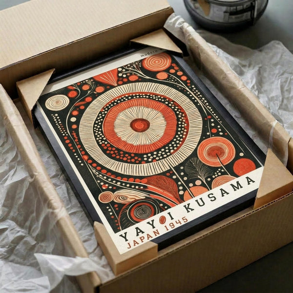 May include: Abstract art print featuring large central circle with radiating lines in orange and cream, surrounded by smaller circular patterns and organic shapes on dark background. Print shown in black frame inside cardboard shipping box with protective paper wrapping, alongside wooden dowels for tube shipping.