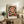 May include: Framed vintage-style poster with large central orange and cream spiral surrounded by smaller circular patterns on dark background, displayed on rustic wooden sideboard beside fern plant, ceramic vase, and stacked books in neutral-toned living room setting