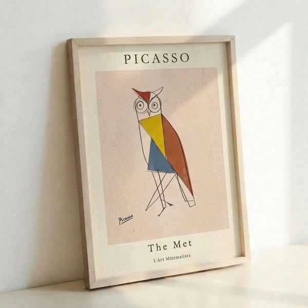 May include: Framed art print featuring a geometric owl in Picasso's minimalist style with colorful sections in red, yellow, blue, and orange against a beige background. The print shows "PICASSO" at top and "The Met L'art Minimaliste" at bottom. Light wood frame sits propped against white wall with soft natural lighting creating gentle shadows.