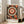 May include: A framed modern art print featuring a large circular mandala design with concentric rings in orange, cream, and black colors, surrounded by decorative dots and spiral patterns. The poster has "YAYOI KUSAMA JAPAN 1945" text at the bottom and displays in a light wood frame, leaning against a white wall next to a beige sofa in a bright living room with large windows.