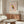 May include: Framed art print featuring a geometric owl in Picasso's style with colorful angular shapes in red, yellow, blue and orange against a pink background. Print hangs above a walnut wood credenza in a minimalist room with white upholstered chair, glass coffee table, and modern lamp. Warm natural lighting creates subtle shadows across the neutral-toned space.