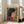 May include: Framed poster print featuring a stylized woman with dark hair in profile, surrounded by colorful flowers on yellow background, displayed on light wooden floors next to a beige upholstered chair near bright windows in a modern living room setting