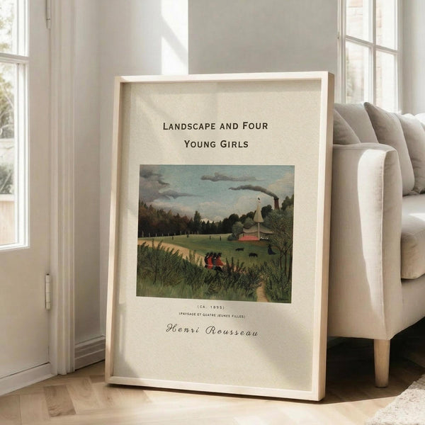 May include: Framed art print leaning against white wall next to beige sofa in bright living room. Print shows Henri Rousseau's 1895 landscape painting with four young girls in red dresses walking through green countryside scene with trees, building, and smoky sky. Light wood frame with cream matting, positioned on wooden floor near windows with natural sunlight streaming in.