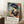 May include: Framed Henri Matisse exhibition poster featuring a woman in a large blue hat and colorful floral dress, painted in vibrant blues, oranges, and greens. The poster displays French text and a Matisse quote about flowers. Shown leaning against a white wall in a bright room setting with natural light, positioned next to a coffee cup on a wooden surface and a cream knitted throw blanket on a white textured rug.