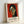 May include: Framed art print featuring a stylized portrait of a woman with geometric facial features in Matisse's distinctive style, set against a vibrant red background. The figure has black hair, elongated neck, and asymmetrical face with bold angular lines. Text below reads "HENRI MATISSE" with French subtitle and quote about flowers. Light wooden frame displayed against white wall, leaning on surface with soft natural lighting creating gentle shadows.