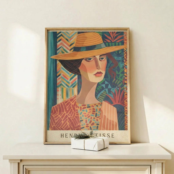 May include: Framed art print featuring a woman in an orange straw hat with geometric patterned background in vibrant blues, oranges, and greens. The colorful poster displays in a light wooden frame on a white wooden shelf alongside a small wrapped gift with pine sprig, against a cream wall in natural lighting.