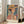 May include: Large framed art print featuring a woman wearing an orange wide-brimmed hat in colorful Art Deco style with geometric patterns in teal, coral, and green tones. The print shows "Henri Matisse Paris" text at bottom and is displayed in a light wooden frame leaning against white walls near a beige upholstered chair in a bright, modern living room with large windows.