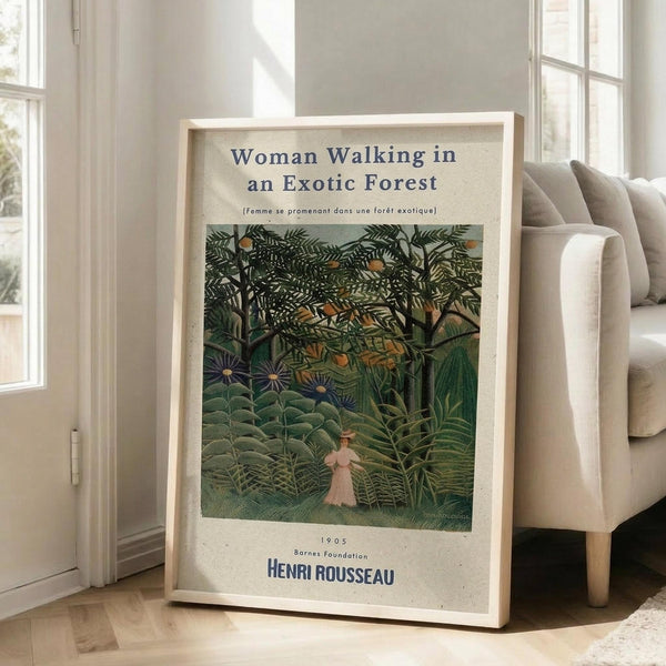 May include: Framed vintage art poster leaning against white wall beside beige sectional sofa. Print shows lush tropical forest scene with dense green foliage, exotic plants, and small figure of woman in pink dress walking through jungle vegetation. Light wood frame on hardwood floors in bright, airy living room with large windows.