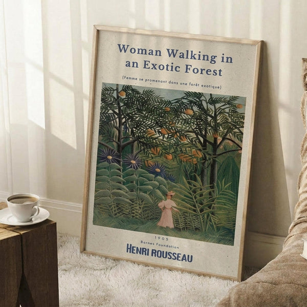 May include: Framed art print of Henri Rousseau's 1905 painting showing a woman in light dress walking through lush jungle scenery with dense green foliage, exotic plants, and tropical trees. Print has cream background with blue text and sits against white paneled wall near wooden side table with white coffee cup and beige textured throw blanket.