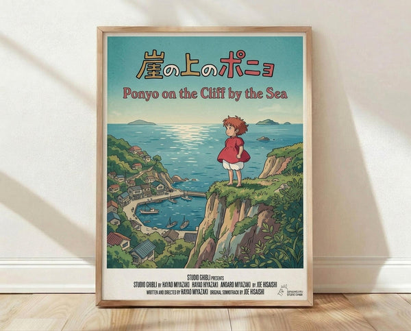 May include: Framed poster print in light wood frame leaning against white wall on wooden floor. Features Studio Ghibli's Ponyo movie poster with young girl in red dress standing on green cliff overlooking blue ocean and coastal village. Japanese and English text at top, Studio Ghibli credits at bottom. Soft natural lighting creates gentle shadows on textured white wall.