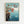 May include: Framed Studio Ghibli Ponyo movie poster print hanging on white wall in light wooden frame. Shows red-haired boy character jumping from rocky coastal cliff into bright blue ocean water with splash effects. Japanese text and "PONYO" title at top against turquoise sky background. Classic anime illustration style with detailed seaside landscape and film credits at bottom.