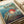 Vintage-style Studio Ghibli movie poster featuring red-haired Ponyo character emerging from splashing ocean water near rocky cliffs. Japanese and English text displays "Ponyo on the Cliff by the Sea" with coastal village in background. Poster has weathered, aged appearance with muted blue and green tones. Print is placed on white surface next to rolled paper tubes, showing realistic scale and texture details.