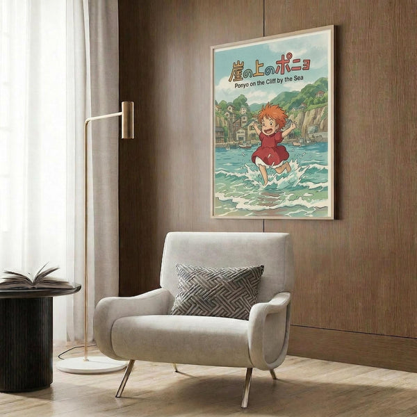 May include: Studio Ghibli Ponyo movie poster in light wood frame hanging on warm brown wood paneled wall above cream upholstered armchair with geometric pillow. Poster shows red-haired child character running through ocean waves with Japanese and English text at top. Modern reading nook setting with brass floor lamp and side table with open book.