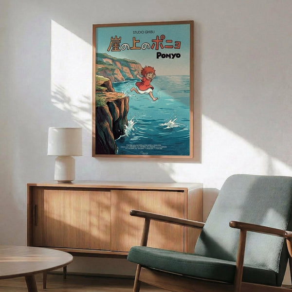 May include: Framed Studio Ghibli Ponyo poster showing red-haired character jumping over ocean cliff, displayed above wooden sideboard with white ceramic lamp and mid-century modern teal armchair in sunlit room with white walls