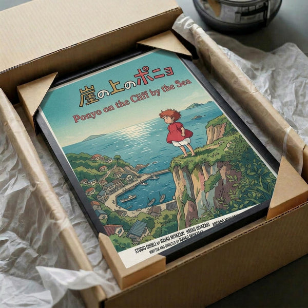May include: Framed Studio Ghibli Ponyo poster in cardboard shipping box with protective wrapping. Artwork shows red-dressed Ponyo character standing on green coastal cliff overlooking seaside village with blue ocean. Japanese and English text at top. Poster has black frame, surrounded by brown cardboard packaging and white tissue paper on wooden surface.