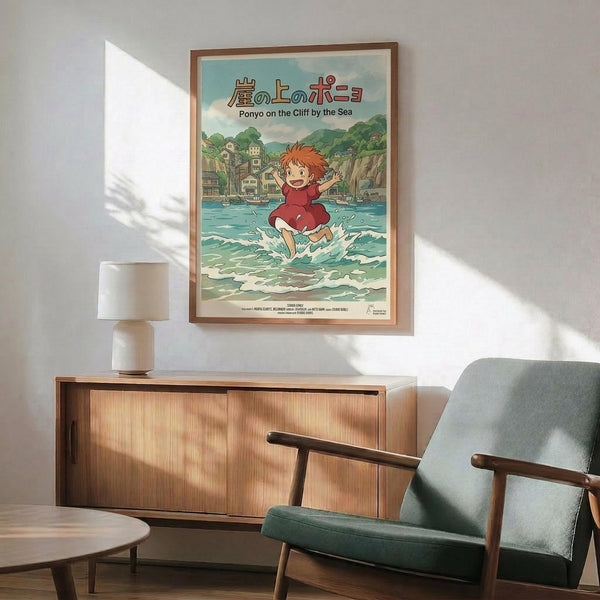 May include: Framed Studio Ghibli Ponyo poster hanging above mid-century modern wooden credenza with white ceramic lamp. Poster shows red-haired child character running through ocean waves with coastal village and cliffs in background. Japanese text at top with English subtitle. Warm wood frame matches furniture. Teal upholstered chair with wooden arms visible in corner. Natural sunlight creates shadows on white wall.