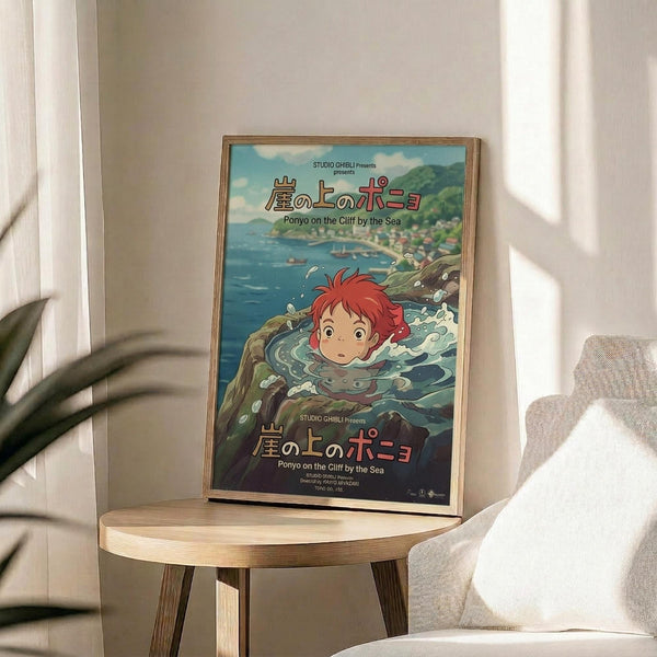 May include: Framed Studio Ghibli Ponyo movie poster featuring red-haired character swimming in ocean waves with coastal village backdrop, displayed on round wooden side table next to beige upholstered chair with throw pillow, plant leaves visible in corner, natural lighting creating soft shadows on neutral wall.