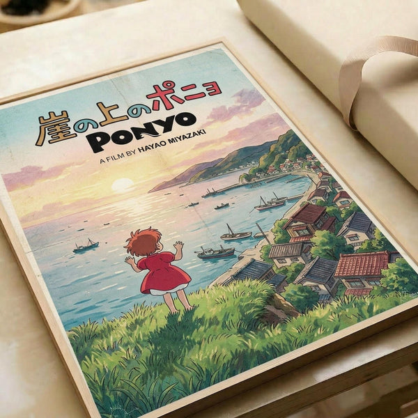 May include: Studio Ghibli-style poster print displayed on white bedding next to a cream pillow. The artwork shows a young girl with red hair in a red dress standing on a grassy cliff overlooking a coastal village with traditional Japanese houses and fishing boats in the harbor. Features soft watercolor-style illustration with pastel sky colors and Japanese text at the top along with "PONYO A FILM BY HAYAO MIYAZAKI" in English lettering.
