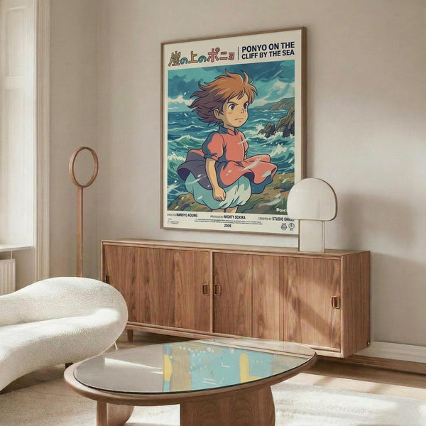 May include: Framed Studio Ghibli Ponyo poster mounted on white wall above mid-century walnut credenza in modern living room. Poster shows red-haired boy character against ocean backdrop with Japanese and English text. Room features cream oval chair, glass coffee table, white dome lamp, and wooden floor lamp with natural lighting.
