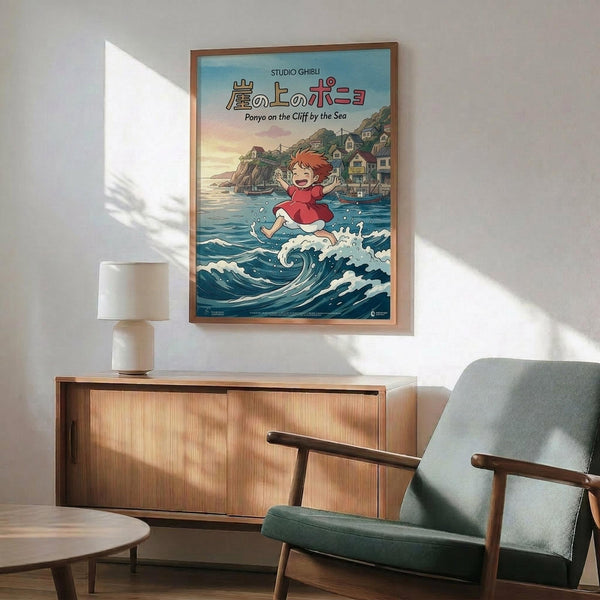 May include: Framed Studio Ghibli Ponyo poster mounted on white wall above wooden sideboard with ceramic lamp. Features animated red-haired girl character running on ocean waves with coastal village in background. Mid-century modern living room setting with teal upholstered armchair, round coffee table, and natural sunlight streaming across scene.