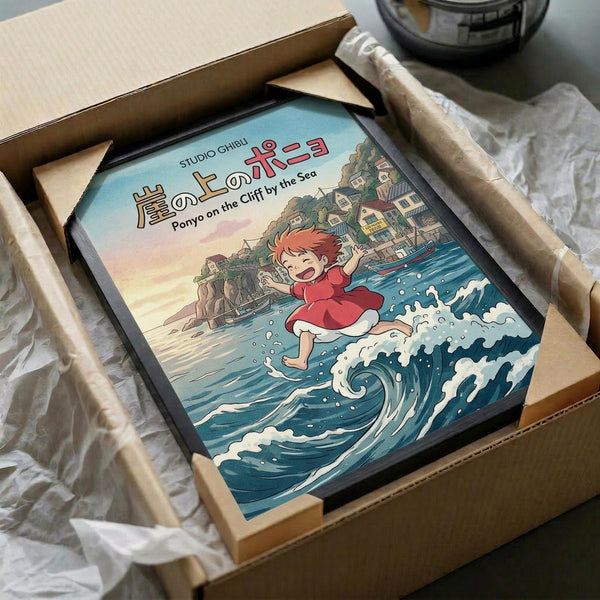 May include: Framed Studio Ghibli Ponyo on the Cliff by the Sea poster in cardboard shipping box with protective wrapping. Artwork shows red-haired Ponyo character running on ocean waves with coastal village on cliffs in background. Illustration features vibrant blues, reds, and warm sunset colors in classic anime art style. Black frame visible inside brown cardboard packaging with white tissue paper.
