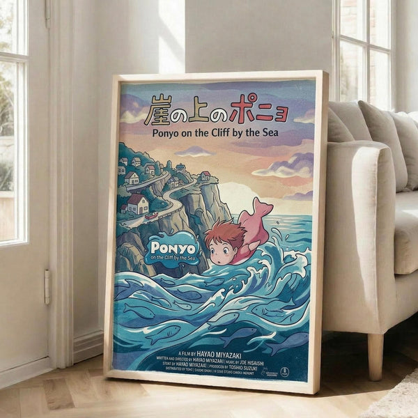May include: Framed poster showing animated character Ponyo swimming in blue ocean waves near clifftop village, with Japanese and English text at top. Colorful illustration features pink-haired character, coastal houses on cliffs, and sunset sky. Light wood frame leans against white wall beside beige sofa in bright room with large windows.